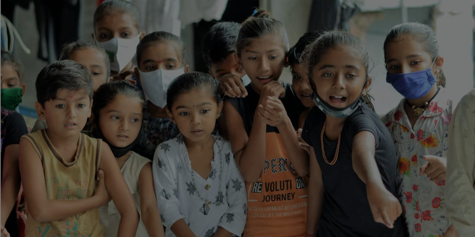 A group of children, several in cloth face masks, crowded together at a village centre in Amreli district