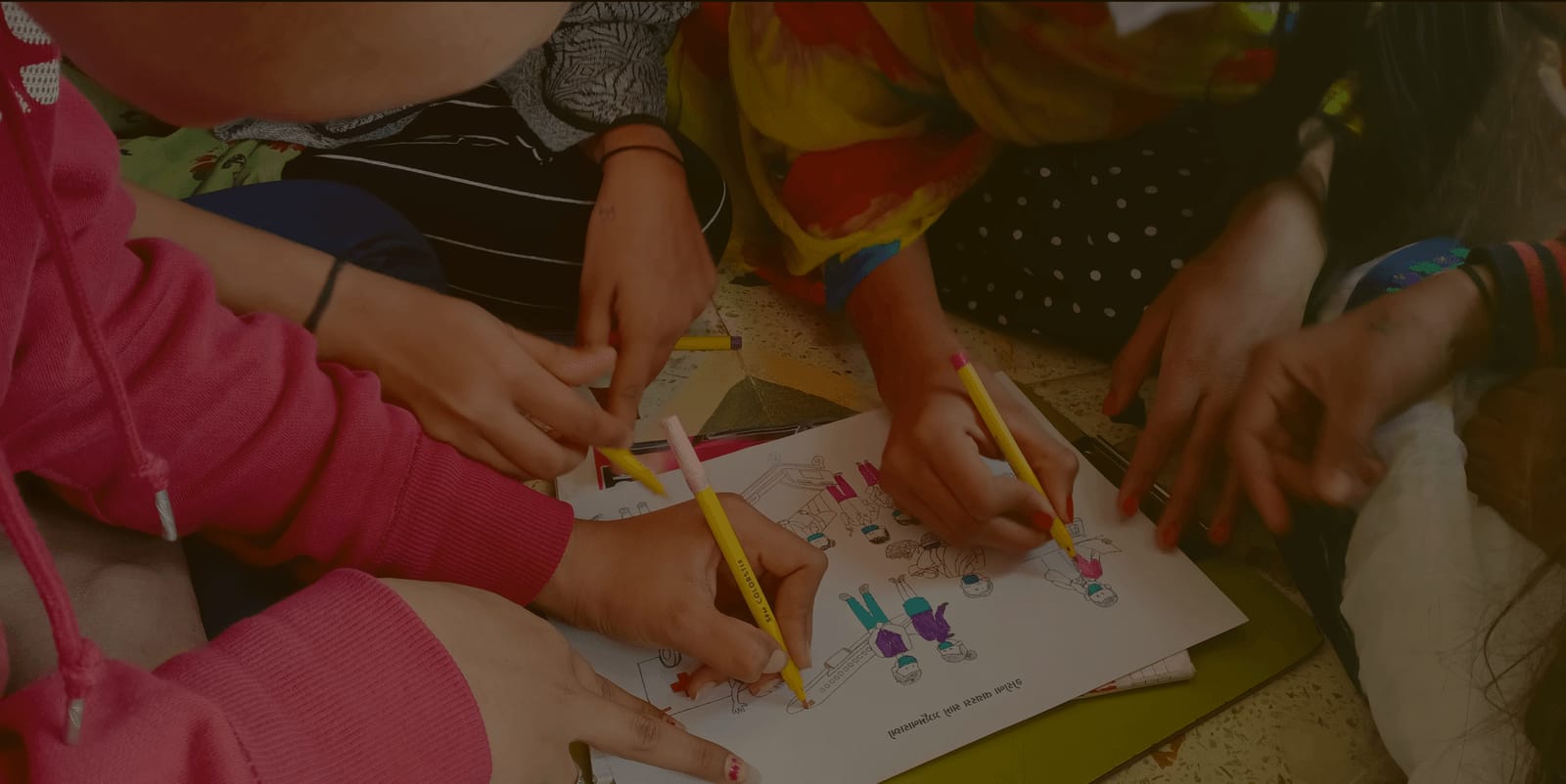 Children's hands colouring a worksheet with pencils, seen from above